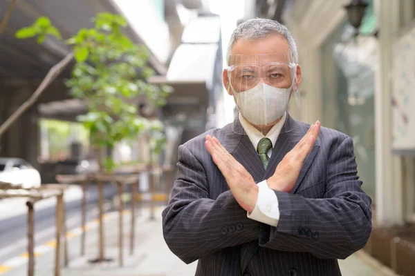 Portrait of mature Japanese businessman with mask and face shield for protection from corona virus outbreak in the city streets