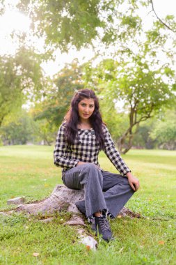 Portrait of young beautiful Indian hipster woman relaxing at the park outdoors