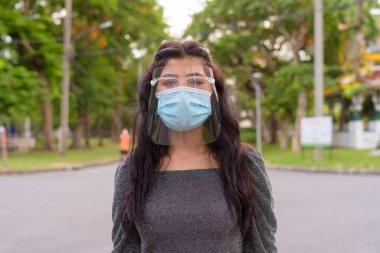 Portrait of young Indian woman with mask and face shield for protection from corona virus outbreak in the streets at the park