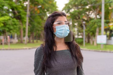 Portrait of young Indian woman with mask and face shield for protection from corona virus outbreak in the streets at the park