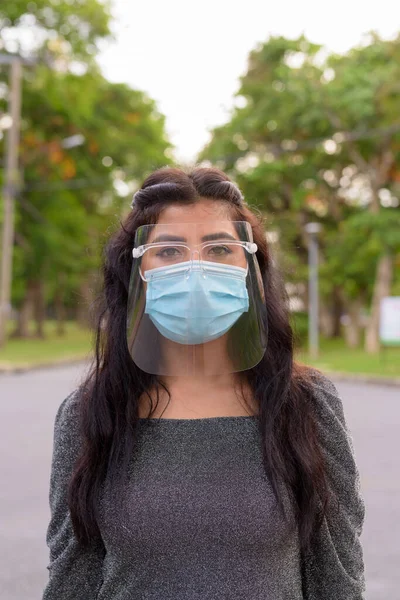 Portrait of young Indian woman with mask and face shield for protection from corona virus outbreak in the streets at the park