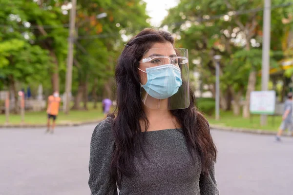 Portrait of young Indian woman with mask and face shield for protection from corona virus outbreak in the streets at the park