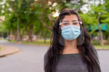 Portrait of young Indian woman with mask and face shield for protection from corona virus outbreak in the streets at the park