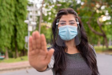 Portrait of young Indian woman with mask and face shield for protection from corona virus outbreak in the streets at the park