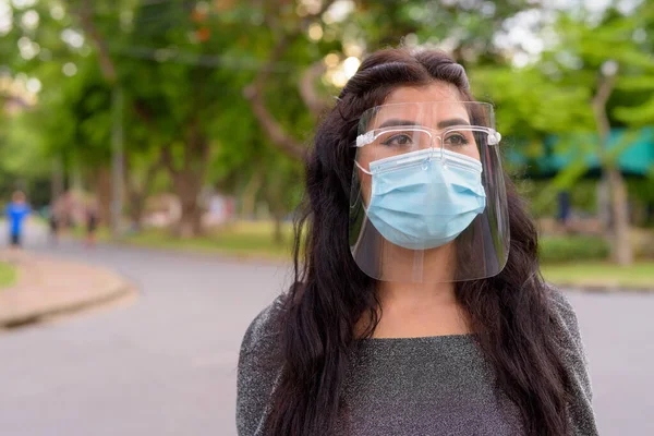 Portrait of young Indian woman with mask and face shield for protection from corona virus outbreak in the streets at the park