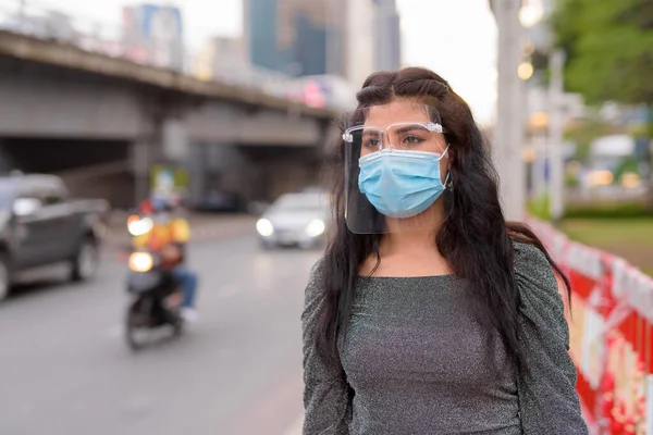 Portrait of young Indian woman with mask and face shield for protection from corona virus outbreak in the city streets outdoors