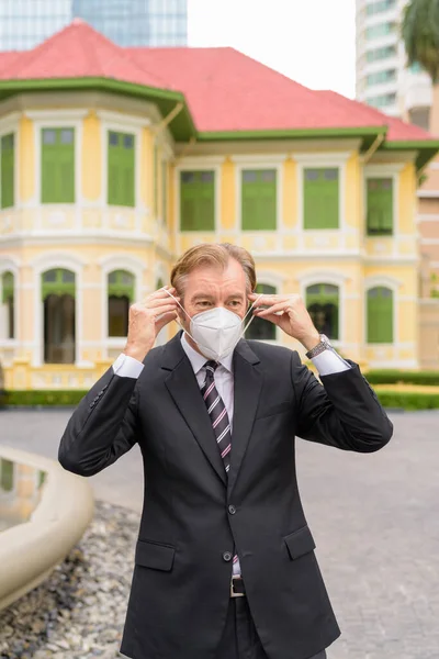 Homme d'affaires mature portant un masque pour la protection contre l'épidémie de virus de la couronne dans la ville en plein air — Photo