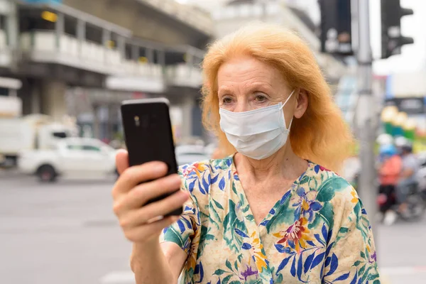Arc szőke idős nő maszk segítségével telefon a városban szabadban — Stock Fotó
