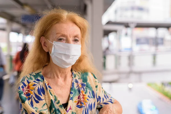 Portret de blonda senior femeie cu masca uita-te la vedere la oraș — Fotografie, imagine de stoc