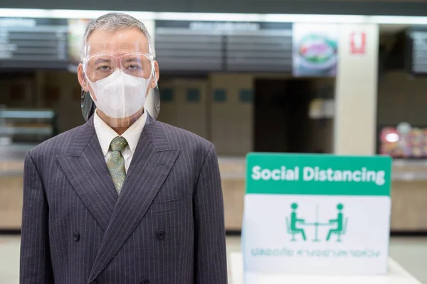 Volwassen japans zakenman met masker en gezicht schild sociale afstand bij food court — Stockfoto