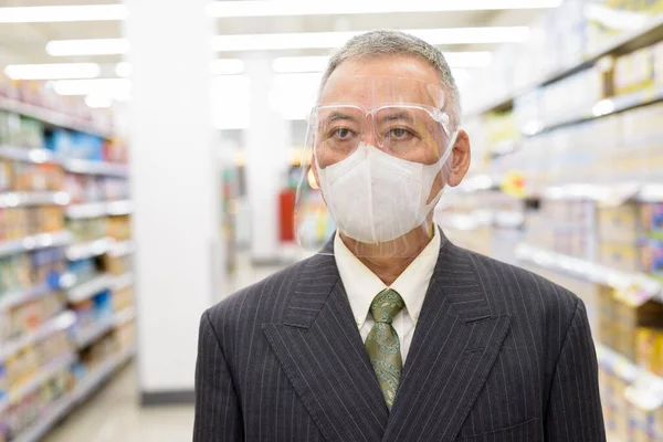 Homme d'affaires japonais mature avec masque et écran facial distance sociale au supermarché — Photo