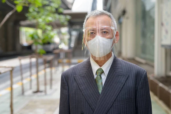 Homme d'affaires japonais mature avec masque et écran facial dans la ville — Photo