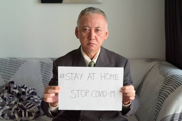 Mature Japanese businessman showing Stay At Home sign for corona virus covid-19 pandemic Stock Photo