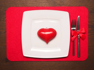 Tahta masada kırmızı kalp şeklinde beyaz bir tabak.