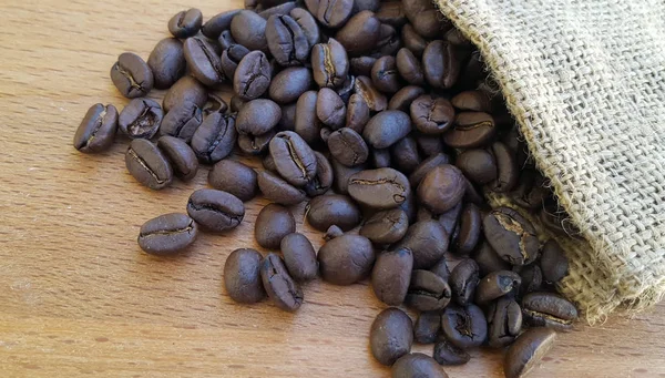 Grãos de café em um saco no fundo de madeira — Fotografia de Stock