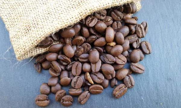 Κόκκους καφέ σε μια τσάντα σε σκούρο φόντο πέτρα — Φωτογραφία Αρχείου