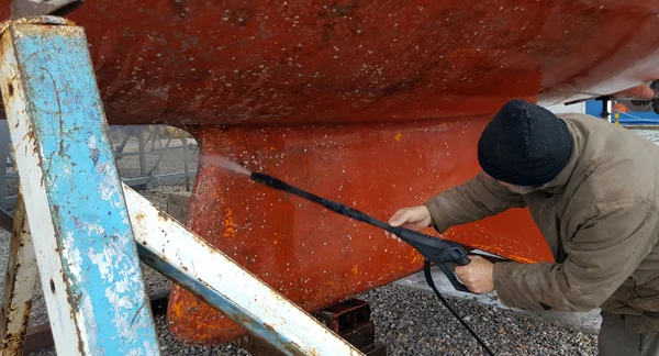 L'uomo pulisce il fondo di una barca a vela con acqua ad alta pressione — Foto Stock