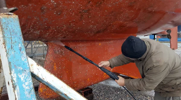 L'uomo pulisce il fondo di una barca a vela con acqua ad alta pressione — Foto Stock