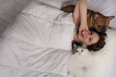 Köpeği ve kedisi olan genç bir kadın sabah yatağında güneşleniyor.