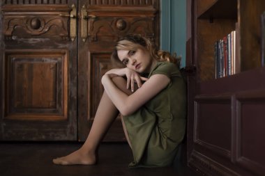 Genç kız odada yerde otururken endişeleniyor.