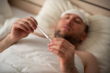 Genç bir adam sıcaktan yatakta yatıyor. Koronovirüs enfeksiyonu olan hasta.