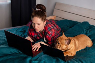 Genç kız ve köpeği Fransız bulldog karantina sırasında laptopun başında çalışıyorlar.