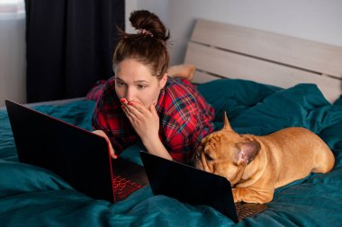 Genç kız ve köpeği Fransız bulldog karantina sırasında laptopun başında çalışıyorlar.