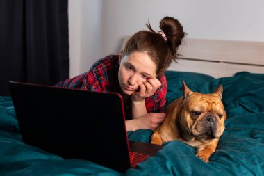 Genç kız ve köpeği Fransız bulldog karantina sırasında laptopun başında çalışıyorlar.