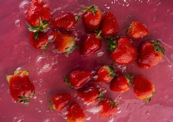 Rijpe Sappige Aardbeien Water Een Rode Achtergrond Rechtenvrije Stockfoto's