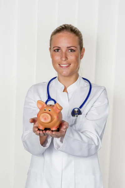 Junge Ärztin mit Sparschwein — Stockfoto