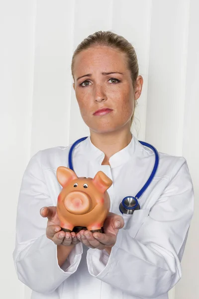 Junge Ärztin mit Sparschwein — Stockfoto