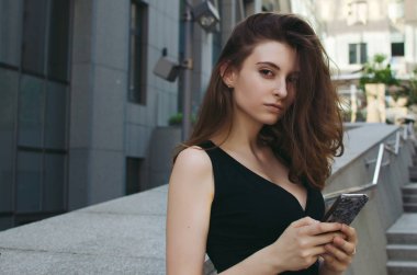 Ofis binaları arka planda, sokakta cep telefonuyla çalışan bir yönetici.