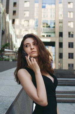 Ofis binaları arka planda, sokakta cep telefonuyla çalışan bir yönetici.