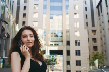 Ofis binaları arka planda, sokakta cep telefonuyla çalışan bir yönetici.