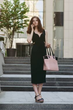 Ofis binaları arka planda, sokakta cep telefonuyla çalışan bir yönetici.