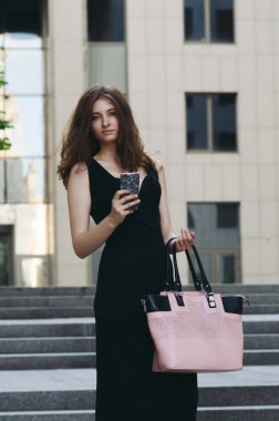 Ofis binaları arka planda, sokakta cep telefonuyla çalışan bir yönetici.