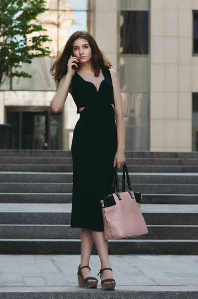 Ofis binaları arka planda, sokakta cep telefonuyla çalışan bir yönetici.