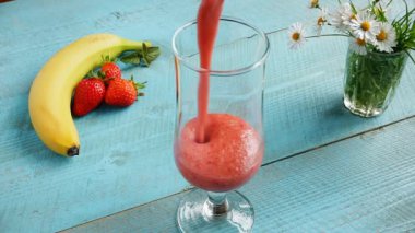 Bir tabloda bir cam bardak çilek muz smoothie dökülür
