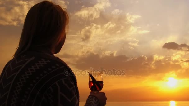 lány ül a parton, nézi a naplementét és forralt bort iszik
