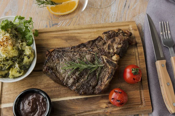 grill beef steak on bones with potatoes and tomatoes on a board t-bone