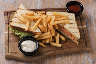 domates jambon peynir ve patates kızartması sosu ile bir tahta üzerinde ızgara sandviç