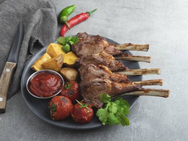 Kızarmış kuzu pirzola, ahşap bir tahtanın üzerinde patates ve domates sosuyla.