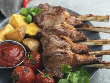 Kızarmış kuzu pirzolası ve kırmızı soslu patates ve domates.