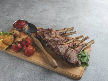 Kızarmış kuzu pirzola, ahşap bir tahtanın üzerinde patates ve domates sosuyla.