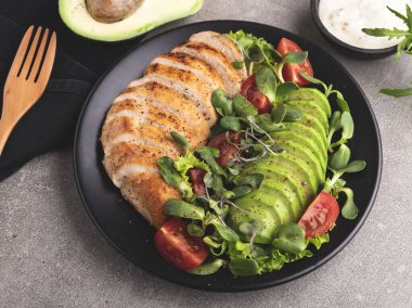 Kızarmış tavuk filetosu, avokado, domates ve sağlıklı besin tabağında otlar.