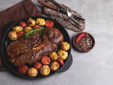 Kemikli ızgara biftek, tavada sarımsaklı fırında patates ve domates.