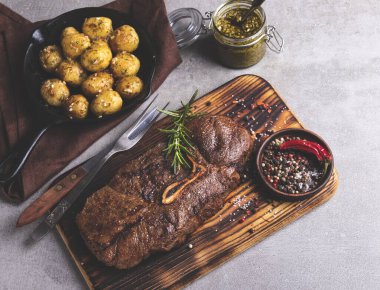 Kesme tahtasında kemikli ızgara biftek, tavada kızarmış patates.