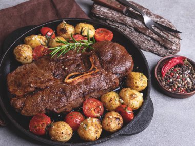 Kemikli ızgara biftek, tavada sarımsaklı fırında patates ve domates.