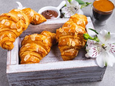 Tahta bir tahtanın üstünde taze taze üç kruvasan dilimlenmiş badem, kahve ve çikolata ezmesi, üst manzara.