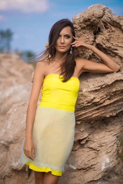 Modische Frau posiert am Strand mit Felsen im Kleid — Stockfoto